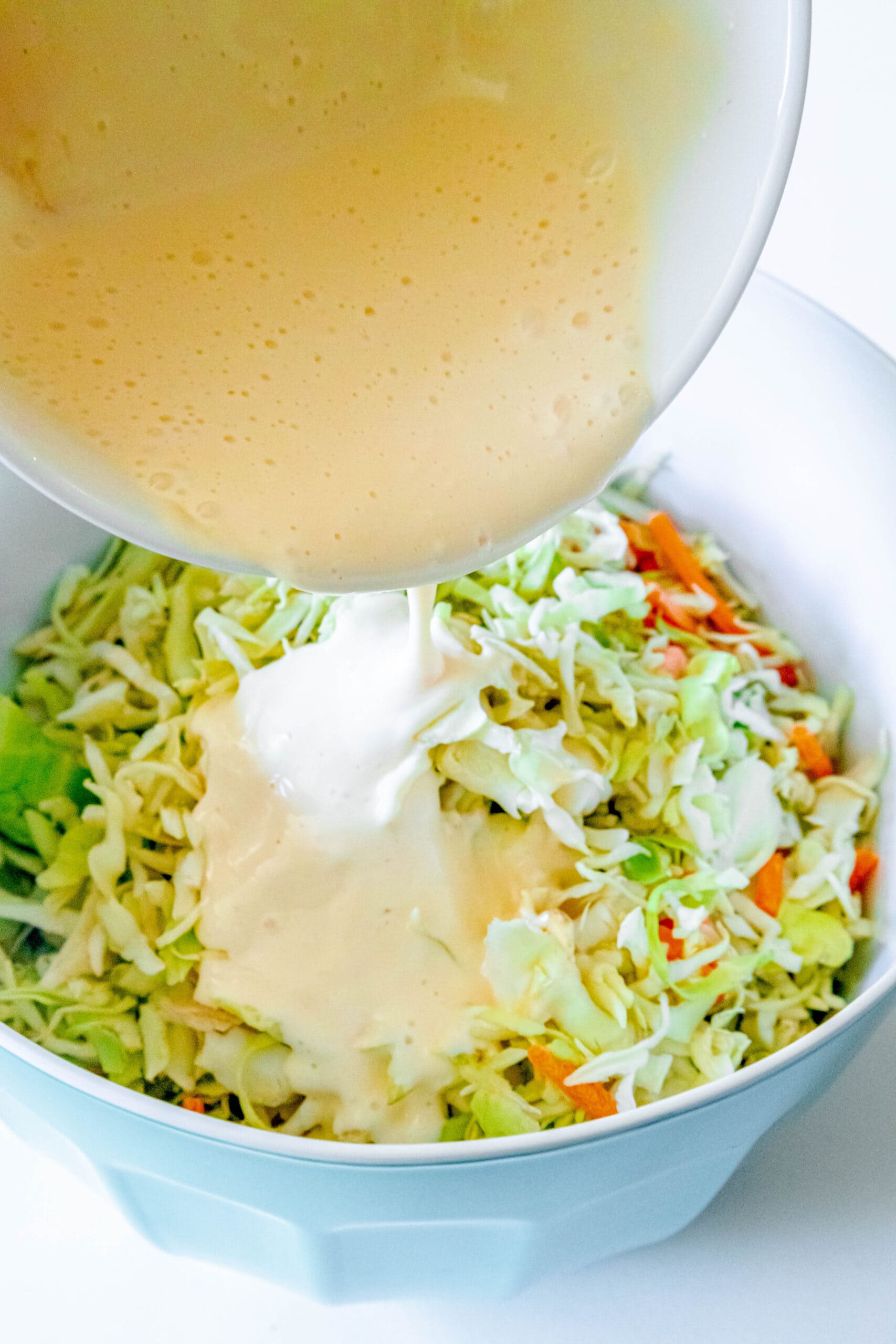 picture of coleslaw dressing being poured into bowl of shredded cabbage