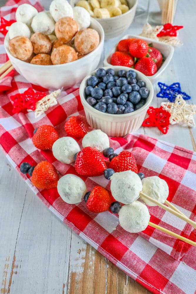 picture of a hand holding a kabob with a donut hole, blueberries, and strawberries on it