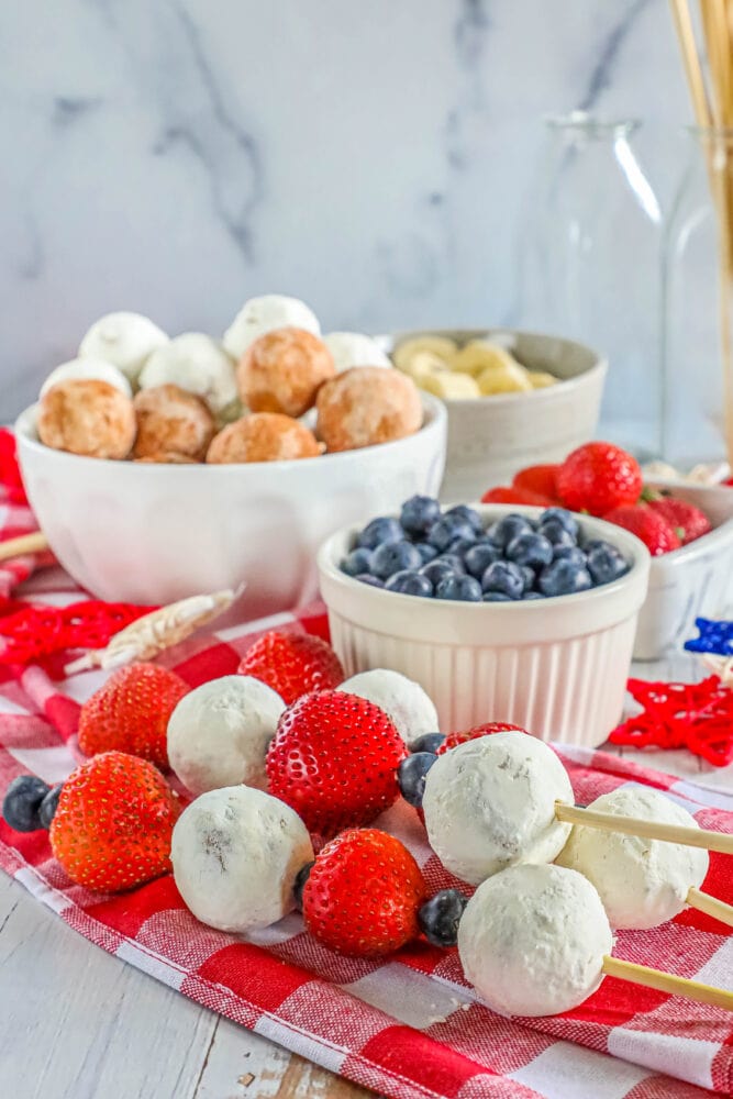 picture of a hand holding a kabob with a donut hole, blueberries, and strawberries on it