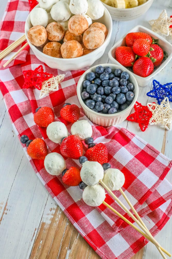 picture of a hand holding a kabob with a donut hole, blueberries, and strawberries on it