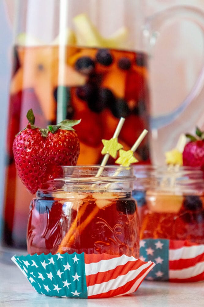 punch with strawberries, blueberries, and apples cut into star shapes in a pitcher and small glasses on a table