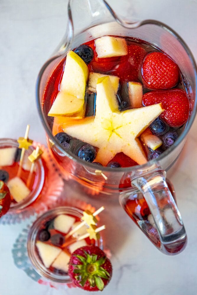 punch with strawberries, blueberries, and apples cut into star shapes in a pitcher and small glasses on a table
