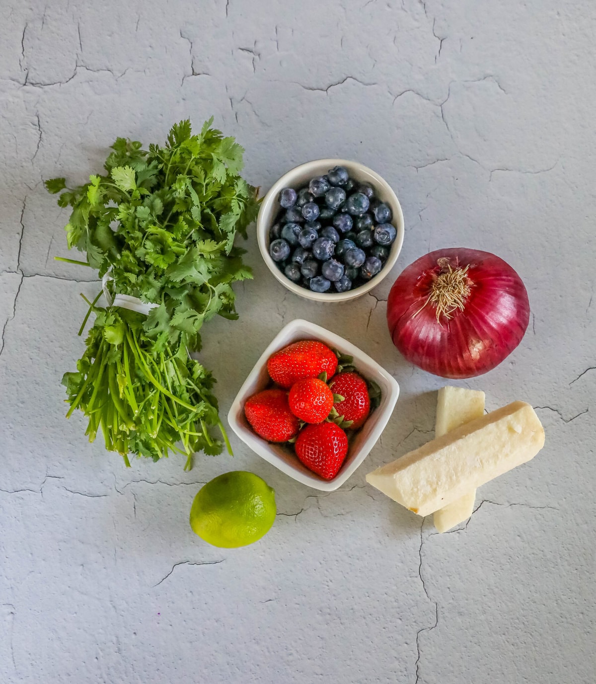 cilantro, blueberries, strawberries, jicama, lime, red onion on a table