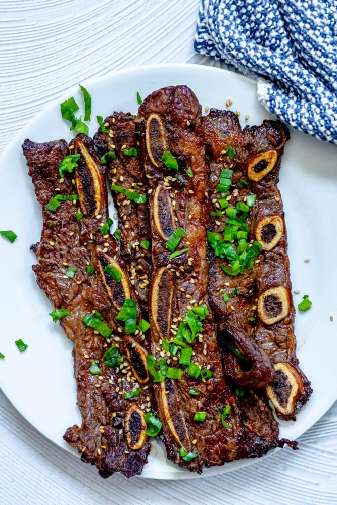 picture of korean grilled flanken ribs topped with green onions and soy seeds on a white plate on a table 