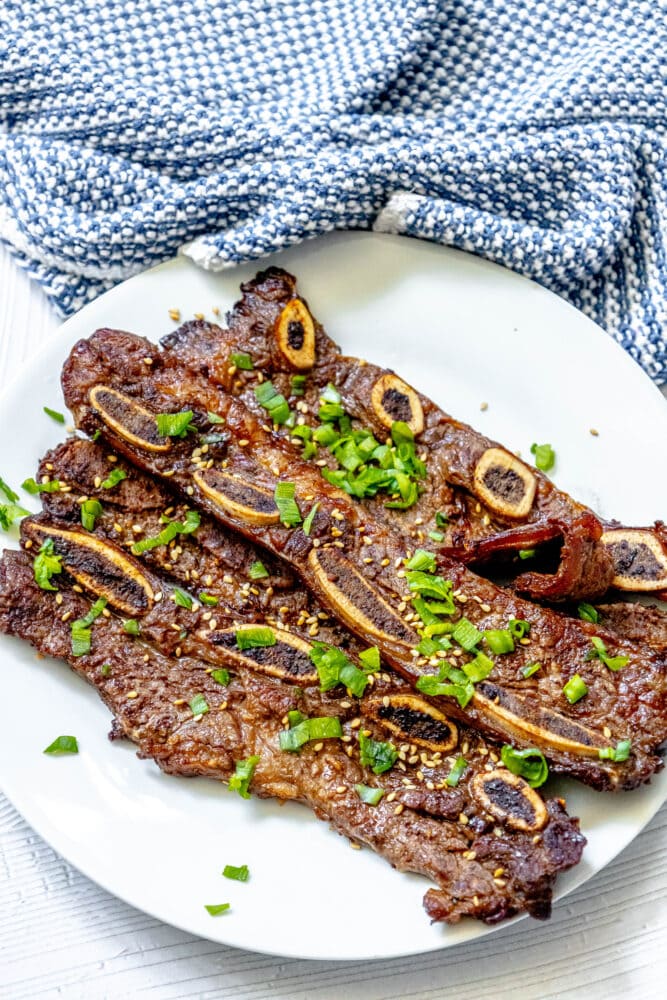 picture of korean grilled flanken ribs topped with green onions and soy seeds on a white plate on a table 