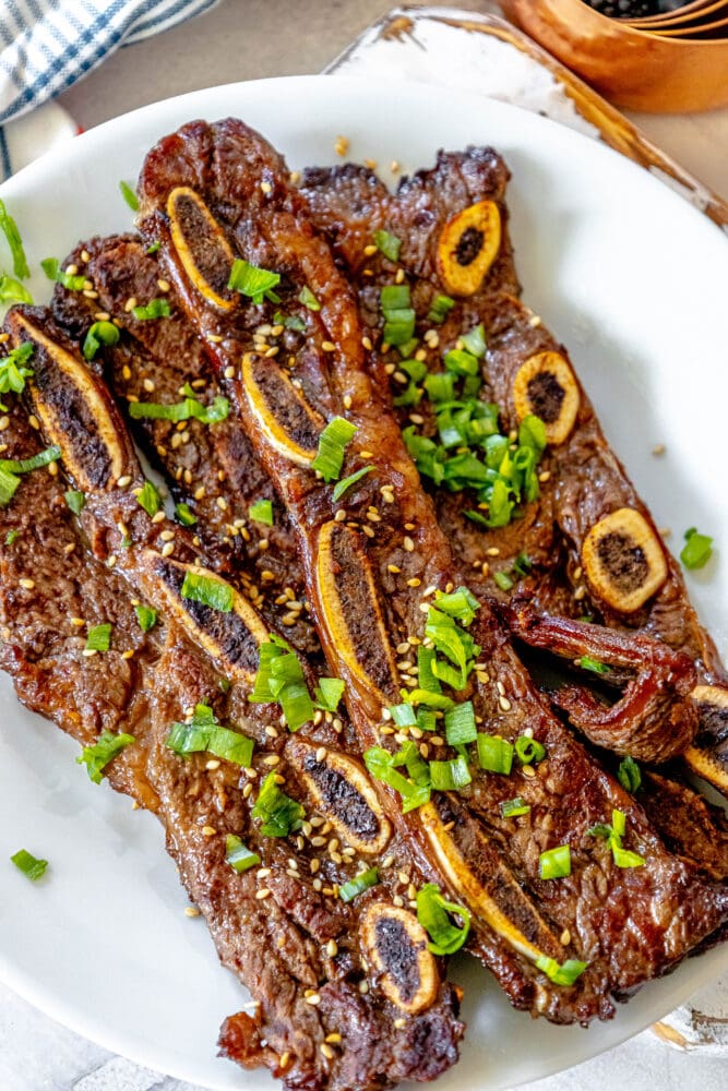 picture of korean grilled flanken ribs topped with green onions and soy seeds on a white plate on a table 