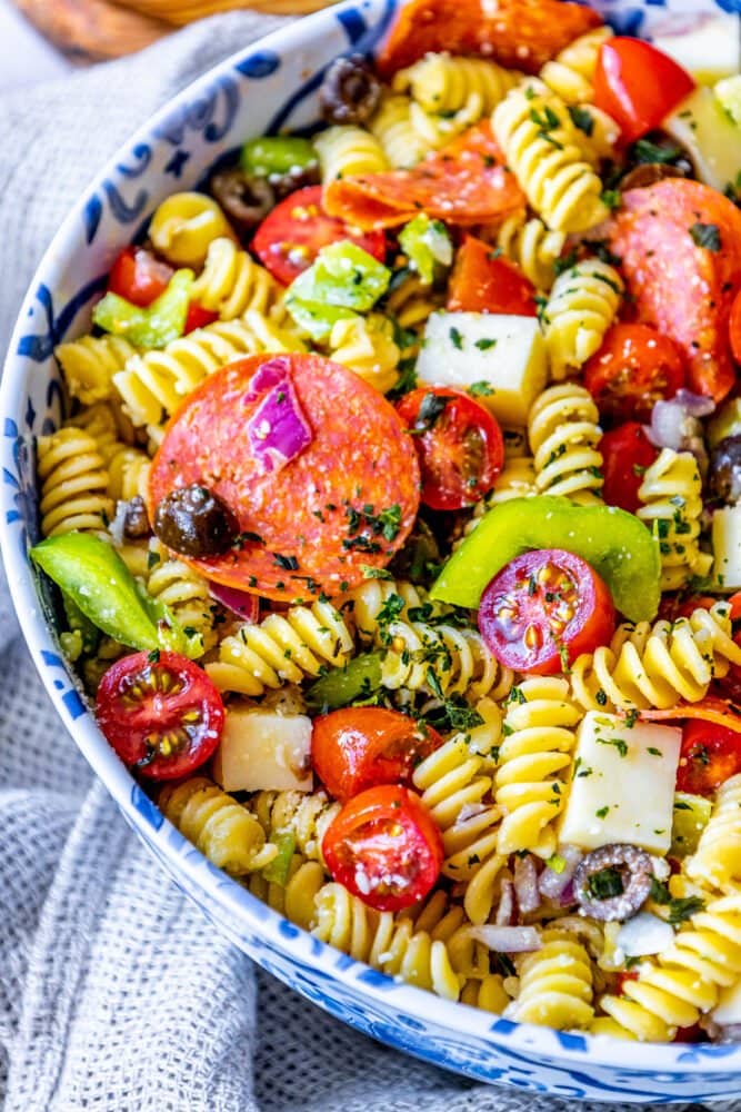 picture of pasta salad with pepperoni, olive, tomatoes, onions, cubes of mozzarella cheese, and bell peppers in a blue bowl 