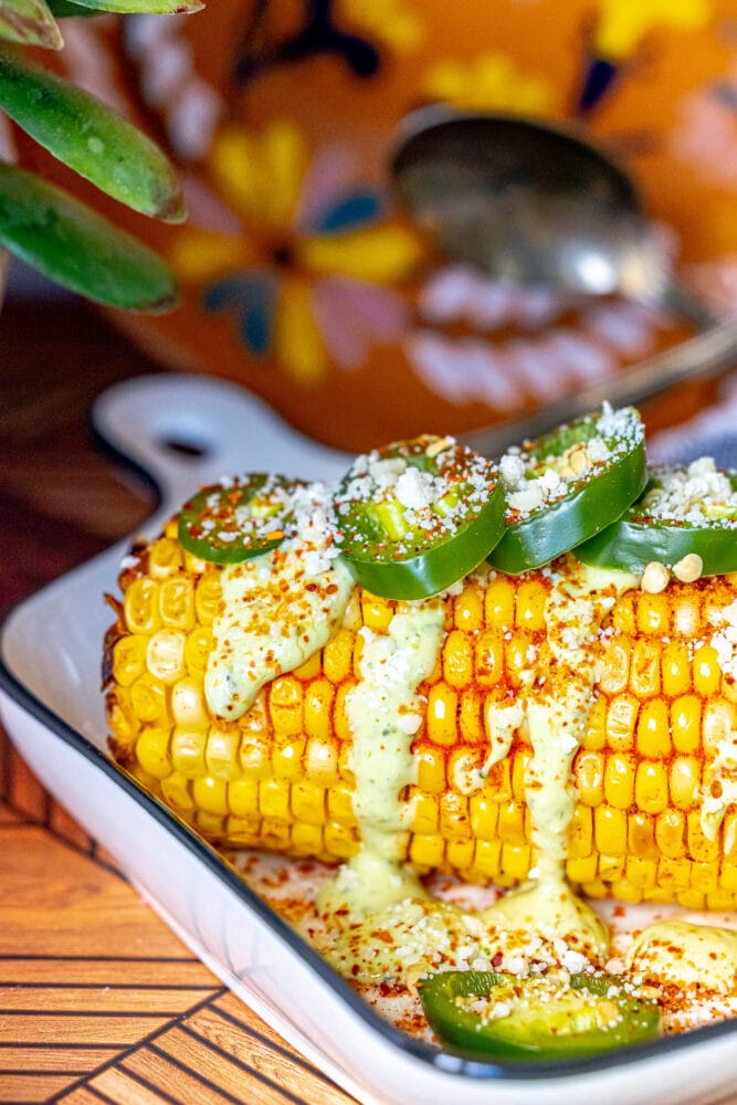 picture of elotes corn cob with crema, cheese, jalapenos, and spices on top