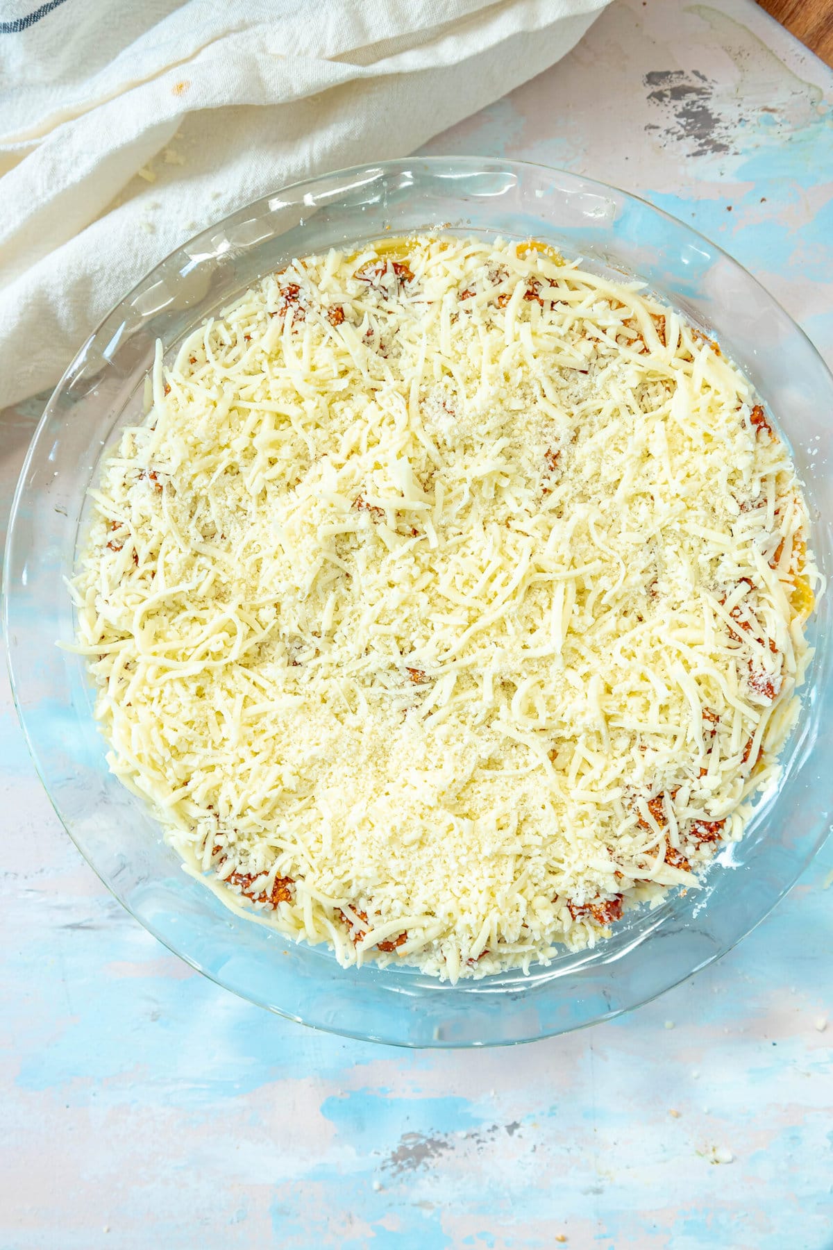 picture of spaghetti pie topped with shredded mozzarella cheese in a pie plate on a table