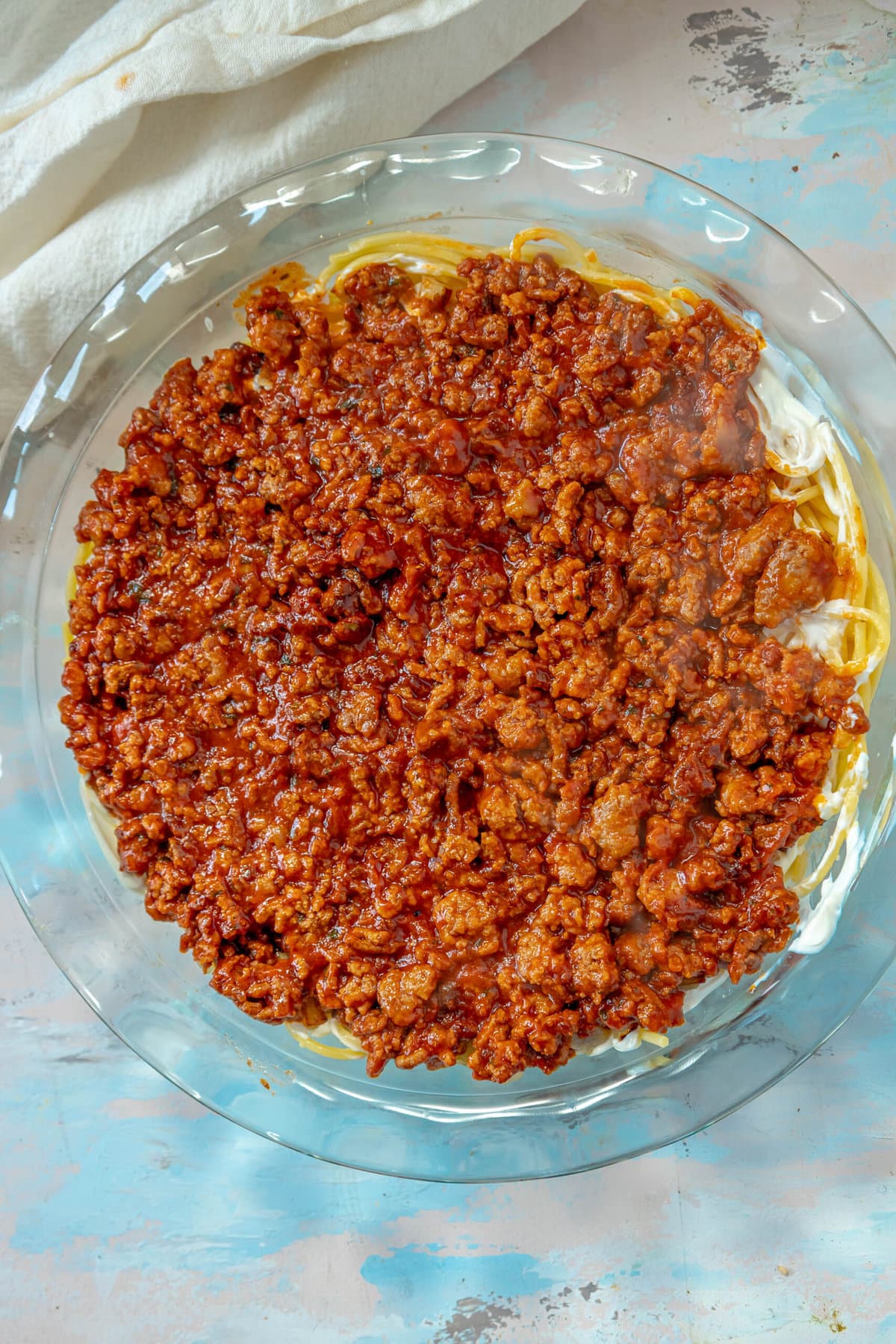 picture of spaghetti pie in a pie plate topped with cooked crumbled meat in tomato sauce in a pie plate