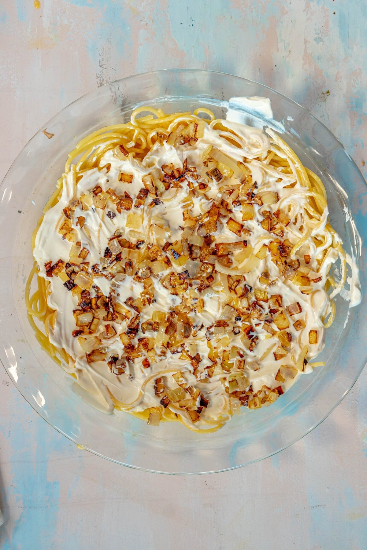 picture of spaghetti and egg mixture topped with sour cream and onions in a pie plate