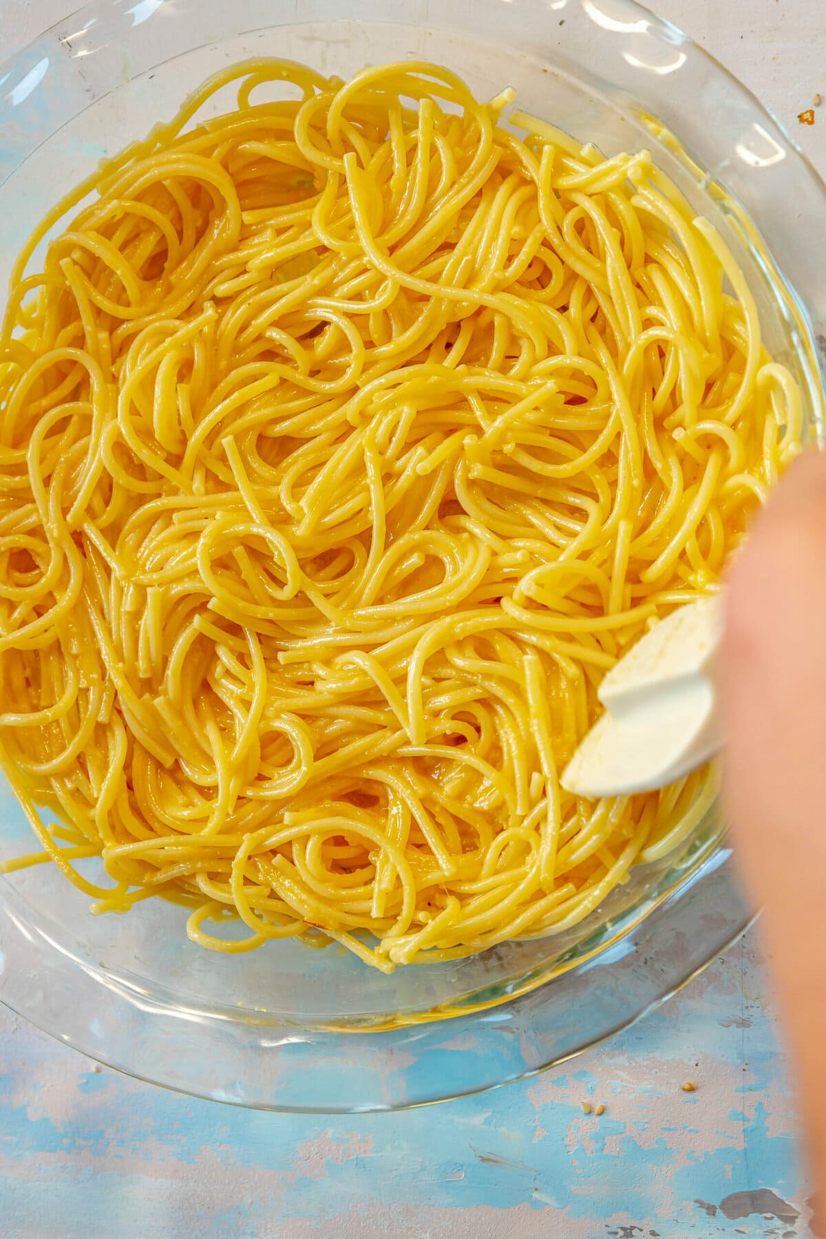 A person using a spatula to stir a bowl of baked spaghetti.