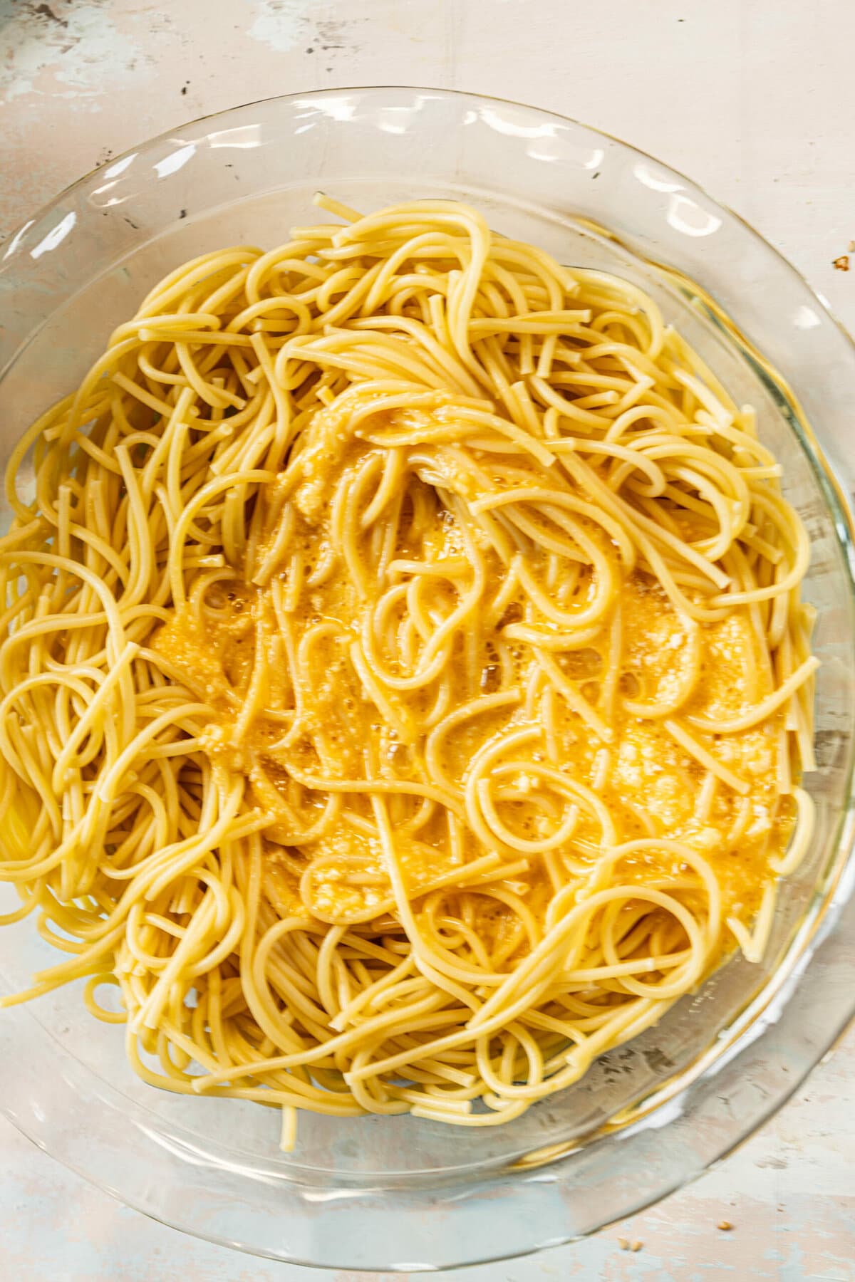 picture of boiled spaghetti in a pie plate with parmesan cheese and eggs mixed in a pie plate