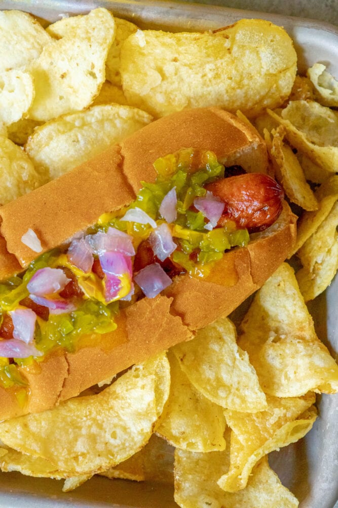 picture of bacon-wrapped hot dog in a bun topped with mustard, relish, and onions