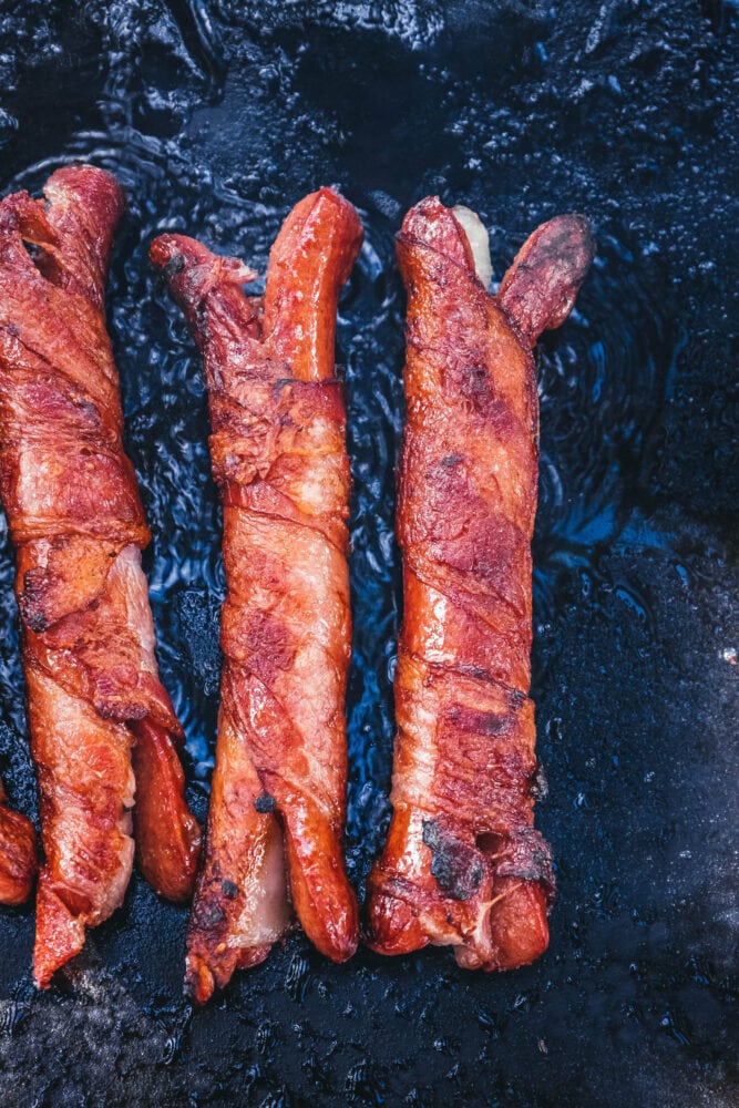 picture of bacon-wrapped hot dogs cooking on a blackstone griddle