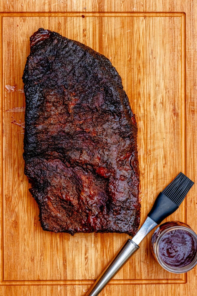 picture of smoked brisket on a wooden cutting board with a brush and bbq sauce next to it