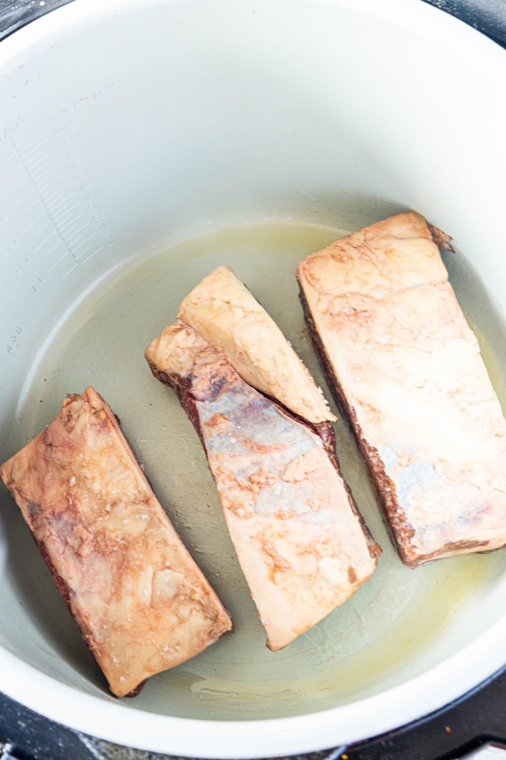 Three pieces of beef short ribs are being cooked in an Instant Pot.