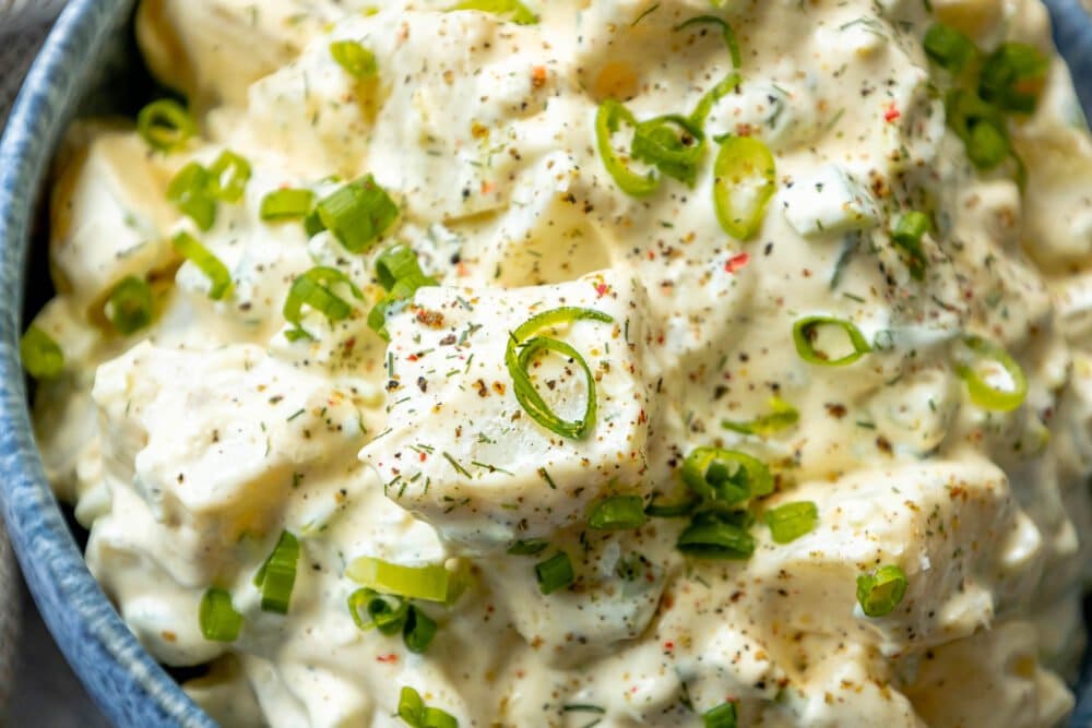 picture of creamy potato salad with green onions and cracked pepper in a blue bowl 