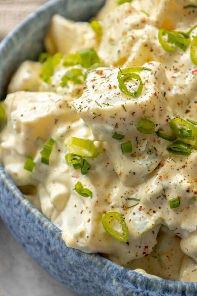 picture of creamy potato salad with green onions and cracked pepper in a blue bowl 