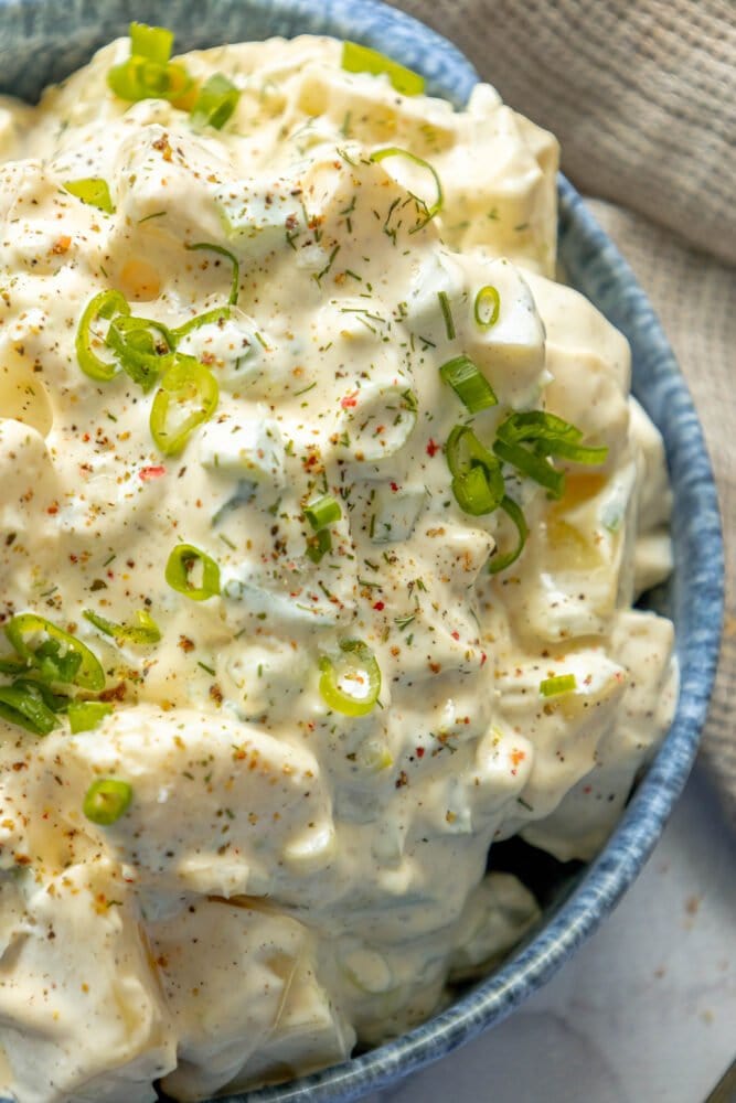 picture of creamy potato salad with green onions and cracked pepper in a blue bowl 