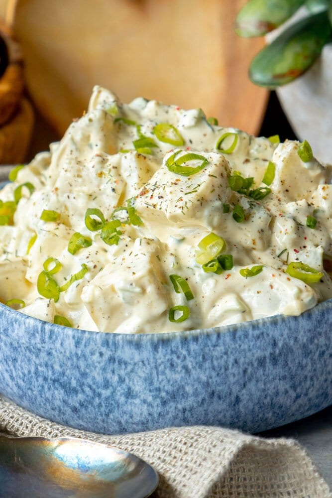 picture of creamy potato salad with green onions and cracked pepper in a blue bowl 