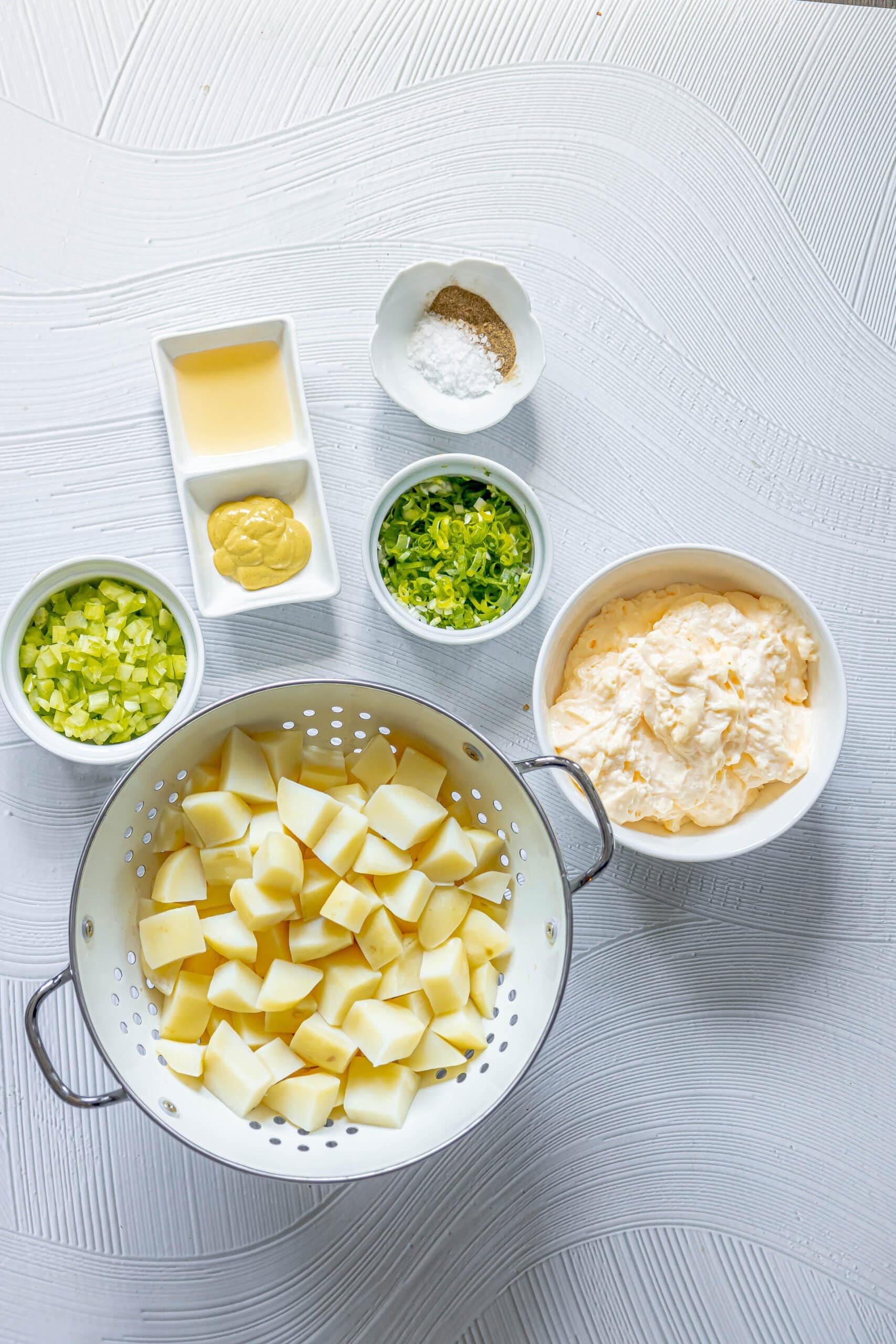 picture of boiled potatoes, mayo, onions, celery, mustard, cider, and seasonings on a table