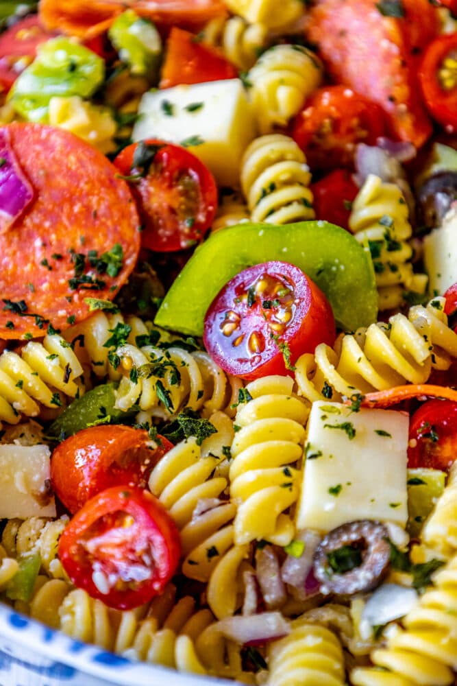 picture of pasta salad with pepperoni, olive, tomatoes, onions, cubes of mozzarella cheese, and bell peppers in a blue bowl 