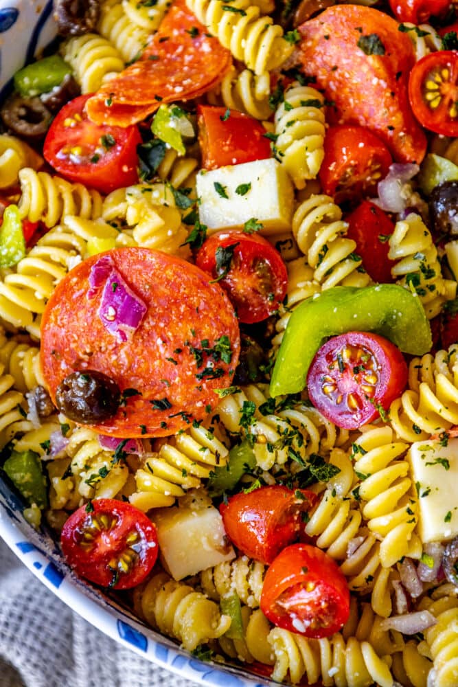 picture of pasta salad with pepperoni, olive, tomatoes, onions, cubes of mozzarella cheese, and bell peppers in a blue bowl 