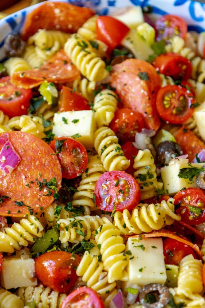 picture of pasta salad with pepperoni, olive, tomatoes, onions, cubes of mozzarella cheese, and bell peppers in a blue bowl 