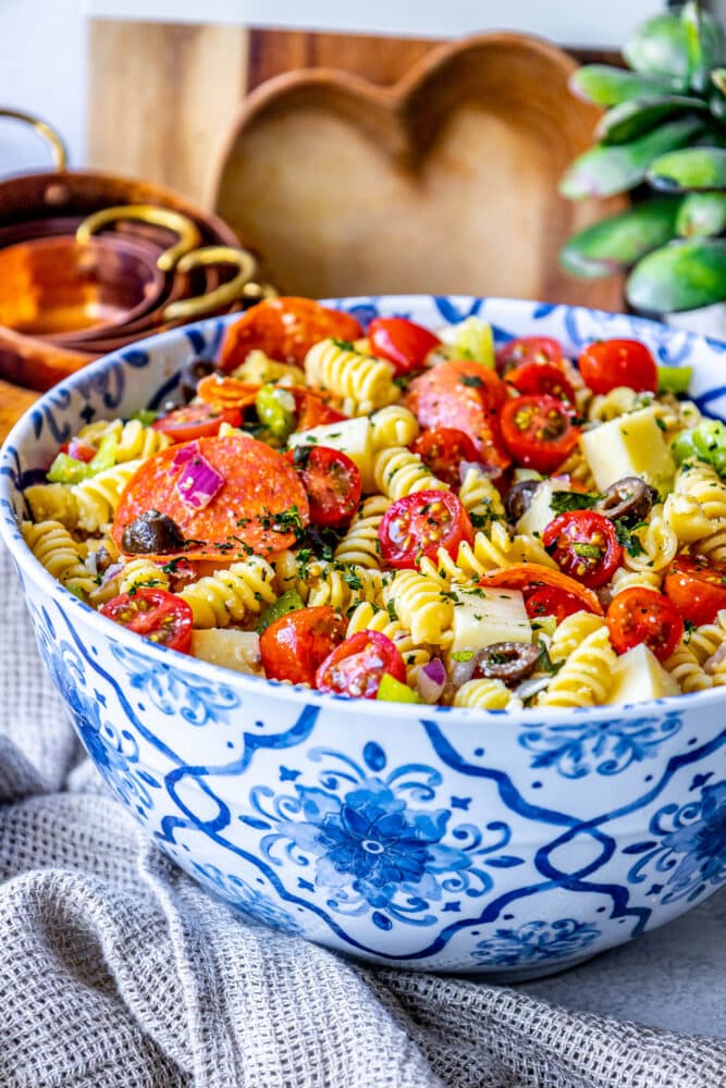 picture of pasta salad with pepperoni, olive, tomatoes, onions, cubes of mozzarella cheese, and bell peppers in a blue bowl 