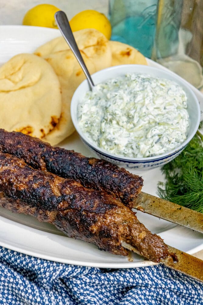 picture of two Greek gyros on skewers on a plate with tzatziki and pita bread on it