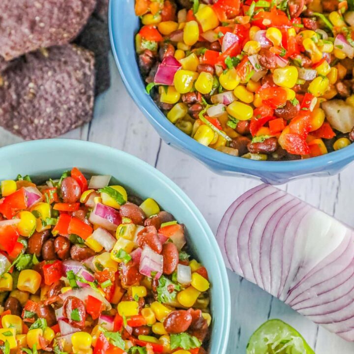 picture of salsa with beans, pepper, onion, corn, and herbs in two blue bowls on a table with chips