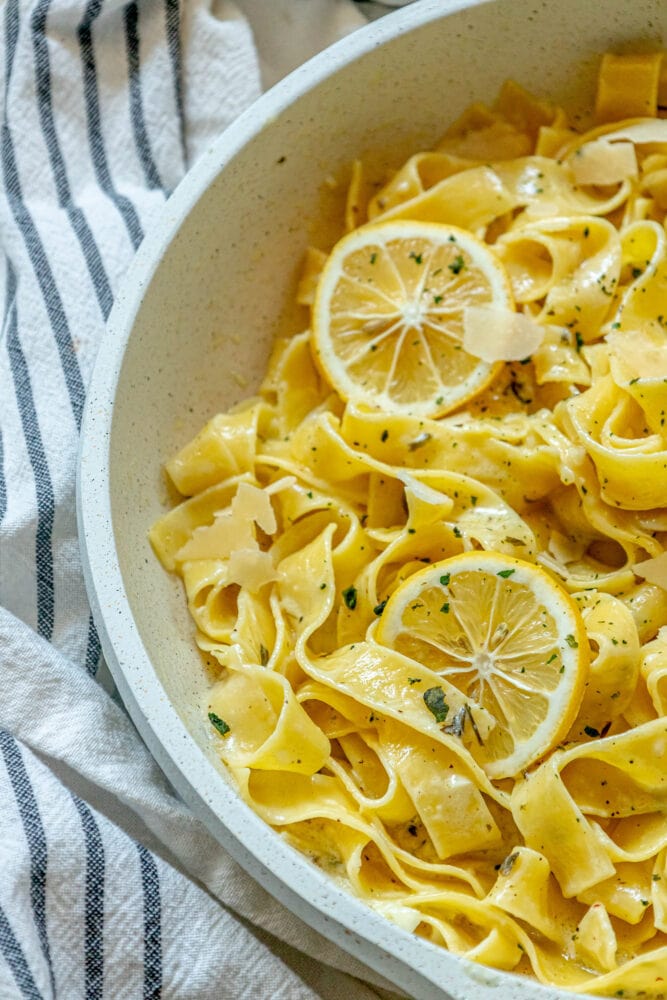 picture of papardelle pasta in a pan with sliced lemons, garlic, cream sauce, and herbs crumbled on top