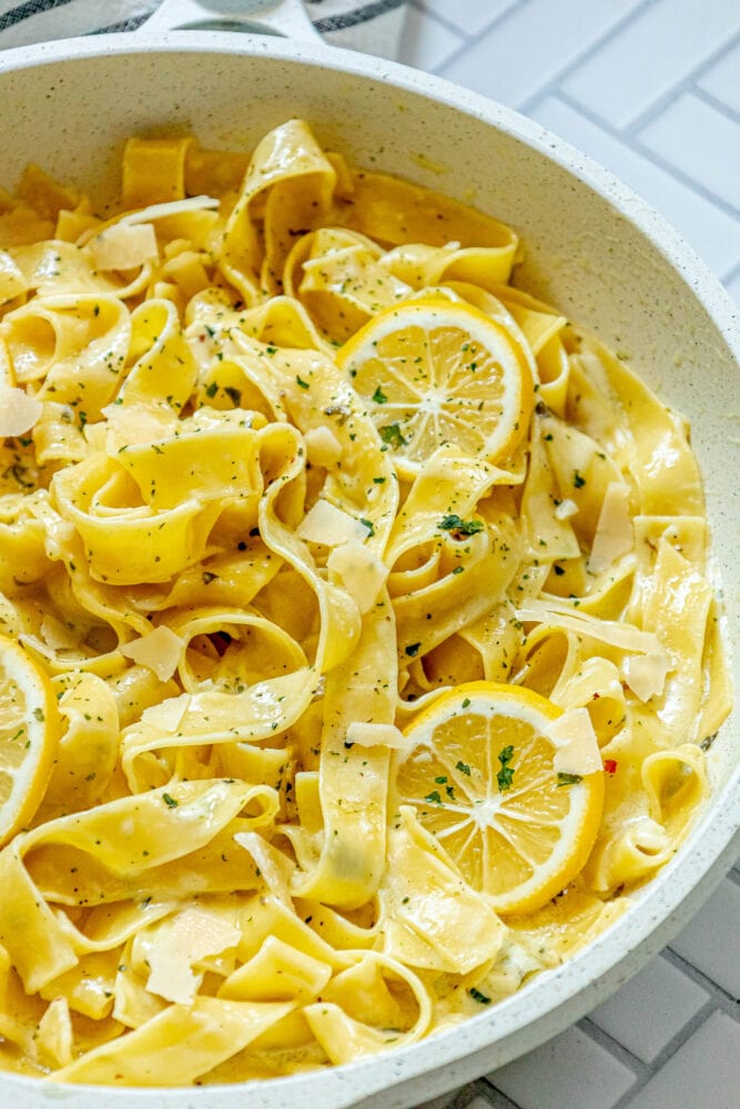 picture of papardelle pasta in a pan with sliced lemons, garlic, cream sauce, and herbs crumbled on top
