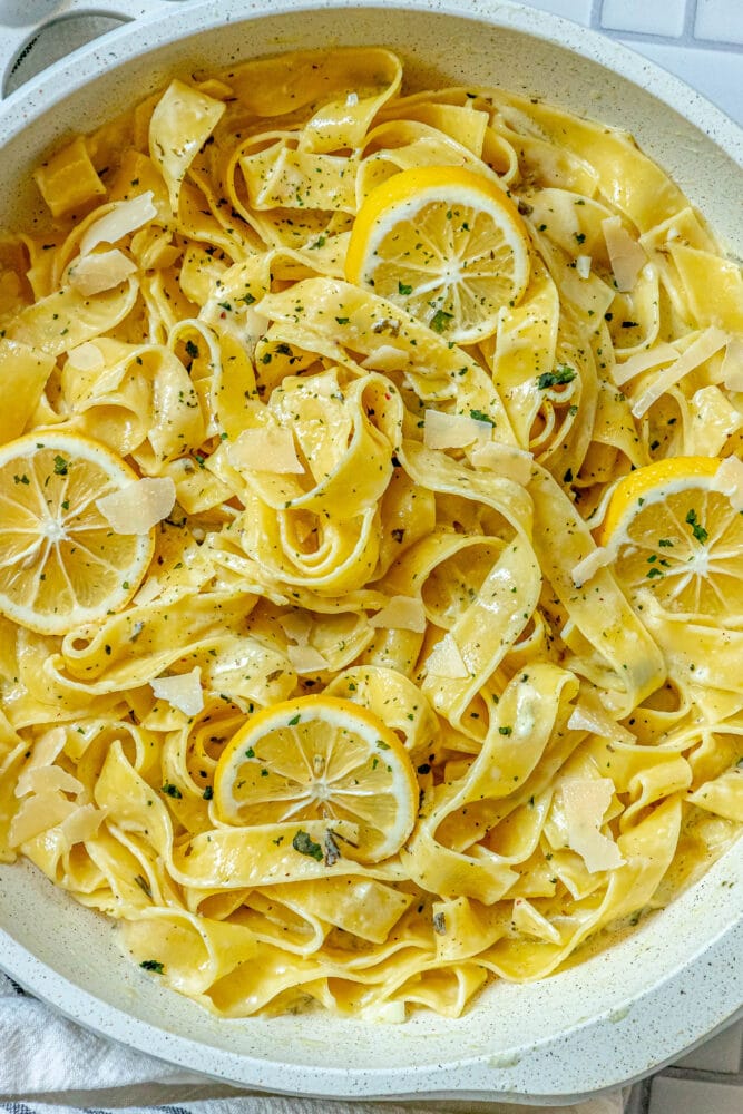 picture of papardelle pasta in a pan with sliced lemons, garlic, cream sauce, and herbs crumbled on top