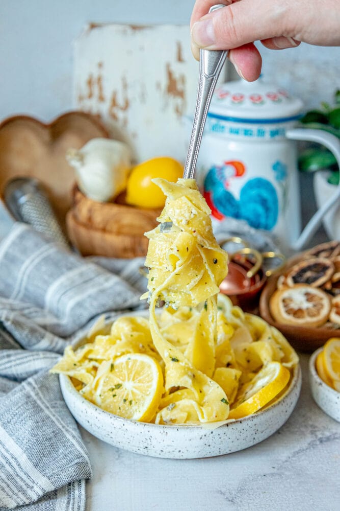 picture of papardelle pasta in a bowl with sliced lemons, garlic, cream sauce, and herbs crumbled on top