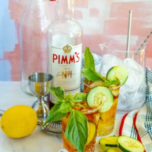 picture of pimms cup cocktails in front of a bottle of pimms with sliced cucumbers on the table