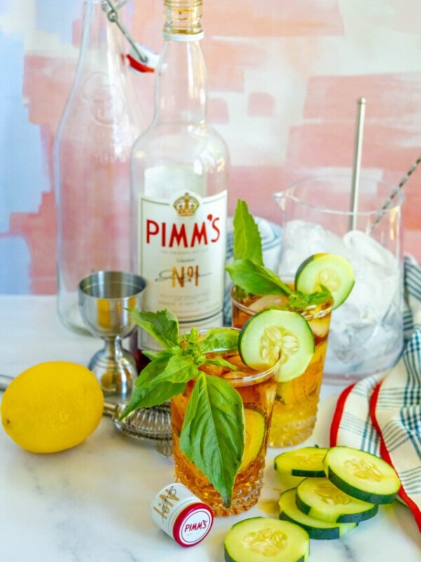 picture of pimms cup cocktails in front of a bottle of pimms with sliced cucumbers on the table