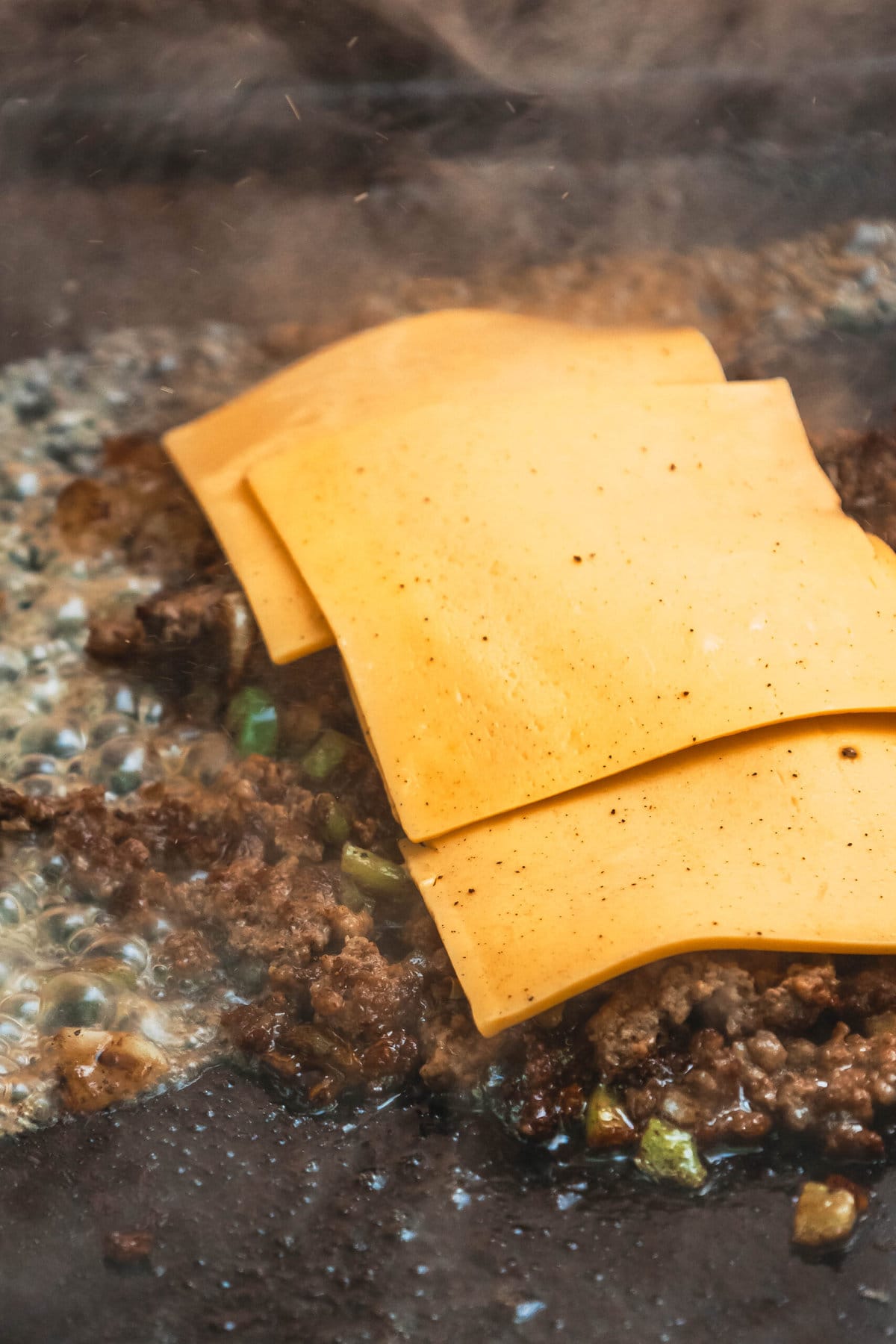 picture of chopped ground beef peppers and onions with cheese on it on a griddle