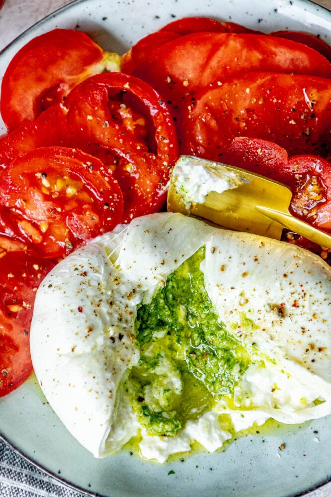 picture of burrata stuffed with pesto sliced open on a plate with sliced tomatoes