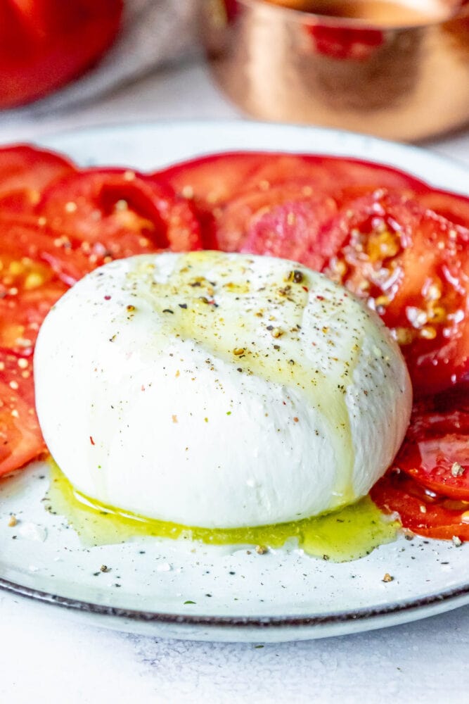 picture of burrata with olive oil salt and pepper drizzled on top on a plate with sliced tomatoes