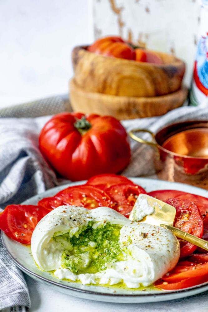picture of burrata sliced open with pesto spilling out on a plate with tomatoes