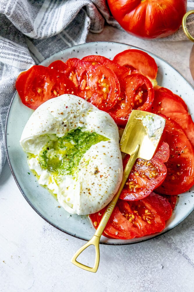 picture of burrata stuffed with pesto sliced open on a plate with sliced tomatoes