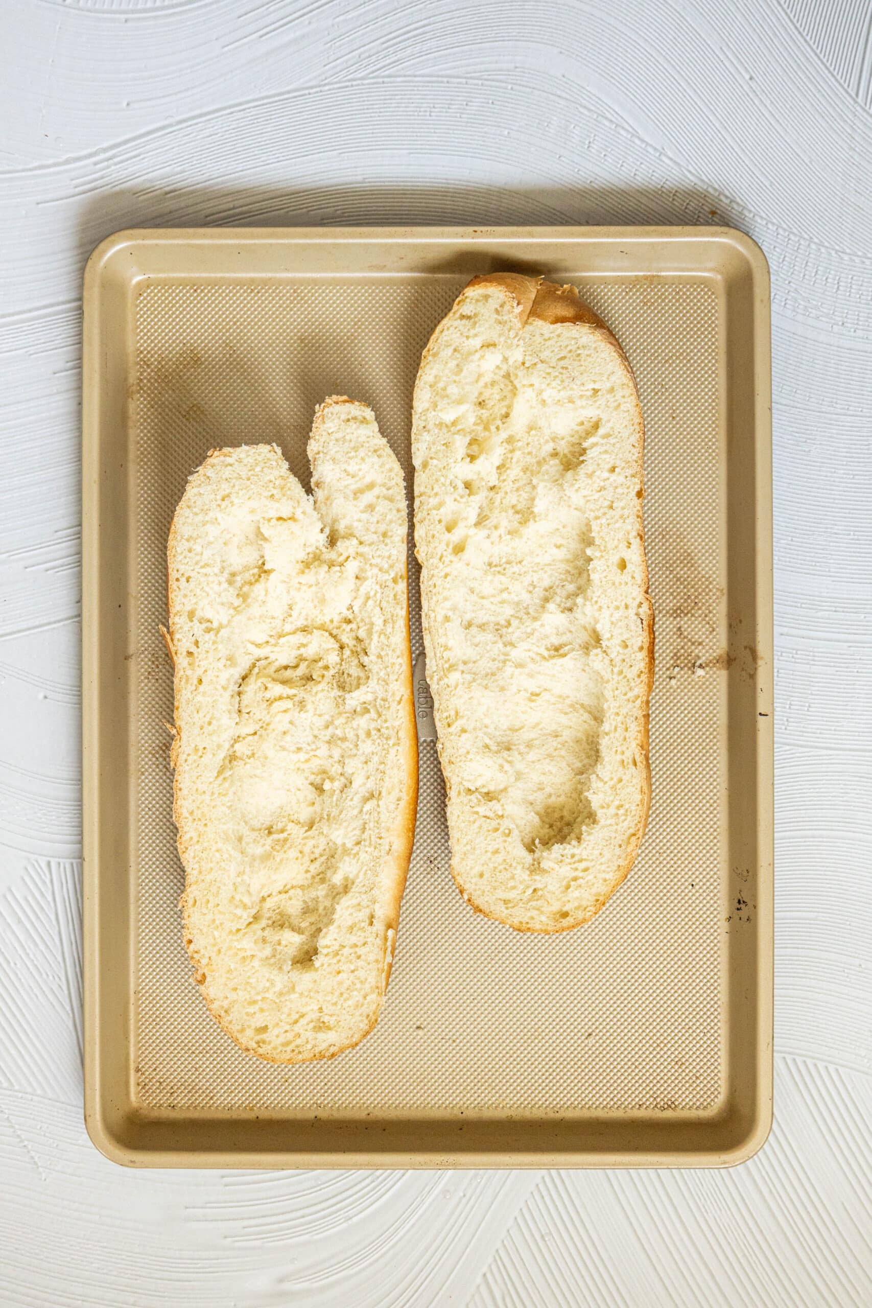 picture of a loaf of french bread cut in half and the middle scooped out on a baking sheet