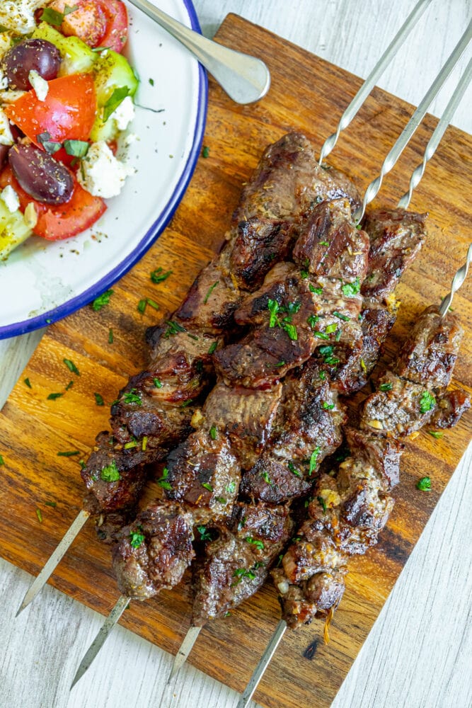 picture of lamb souvlaki on a skewer on a wood cutting board with chopped cilantro on top