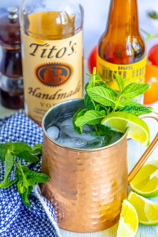 moscow mule in a copper cup with mint and limes in it on a table