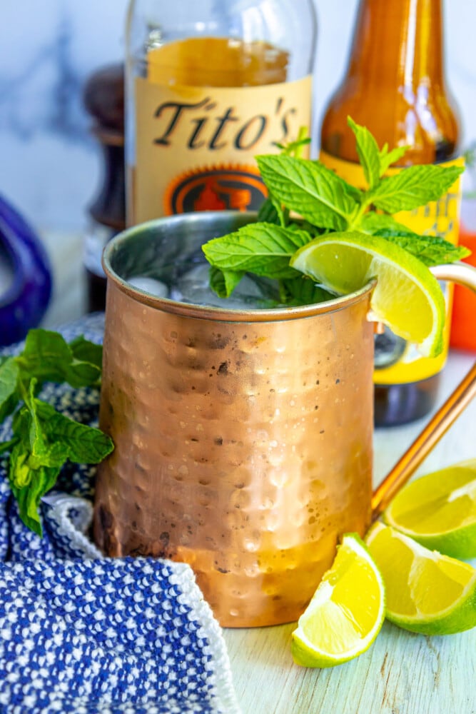 picture of moscow mule in a copper cup with mint and limes in it on a table