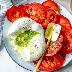 picture of burrata sliced open with pesto spilling out on a plate with tomatoes