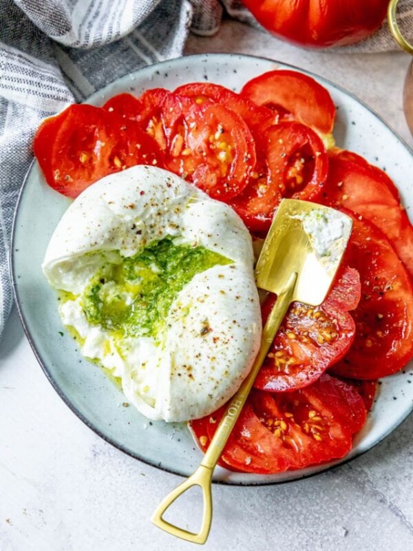 picture of burrata sliced open with pesto spilling out on a plate with tomatoes