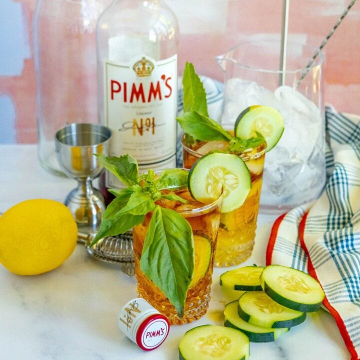pimms cup cocktails in front of a bottle of pimms with sliced cucumbers on the table